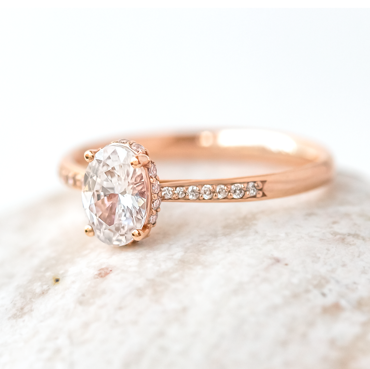 An oval-cut moissanite engagement ring with a hidden halo effect, set in a gold band, displayed on a white marble surface.