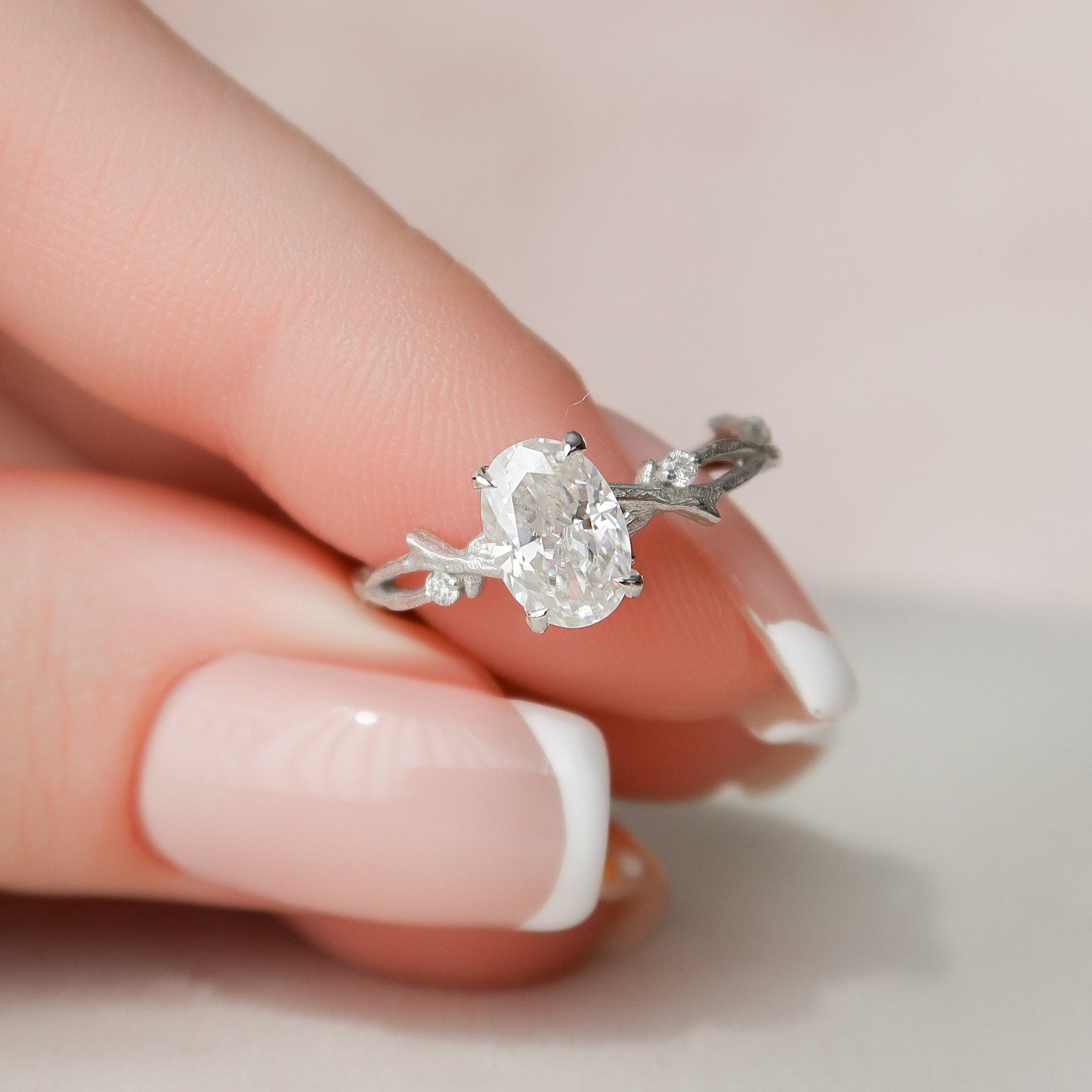 A woman's hand holding an oval-cut twig moissanite engagement ring with a gold band.