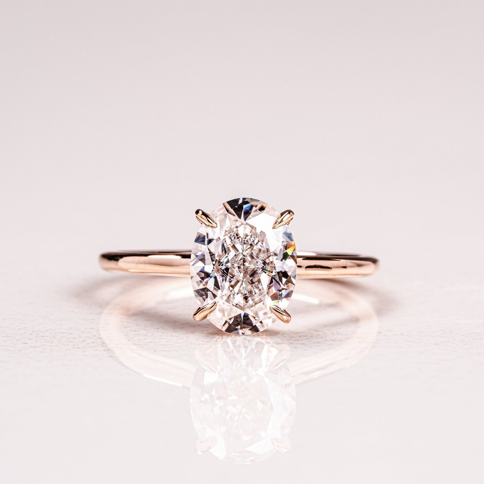 A solitaire engagement ring with a hidden halo setting, featuring an oval-cut moissanite gemstone on a gold band.