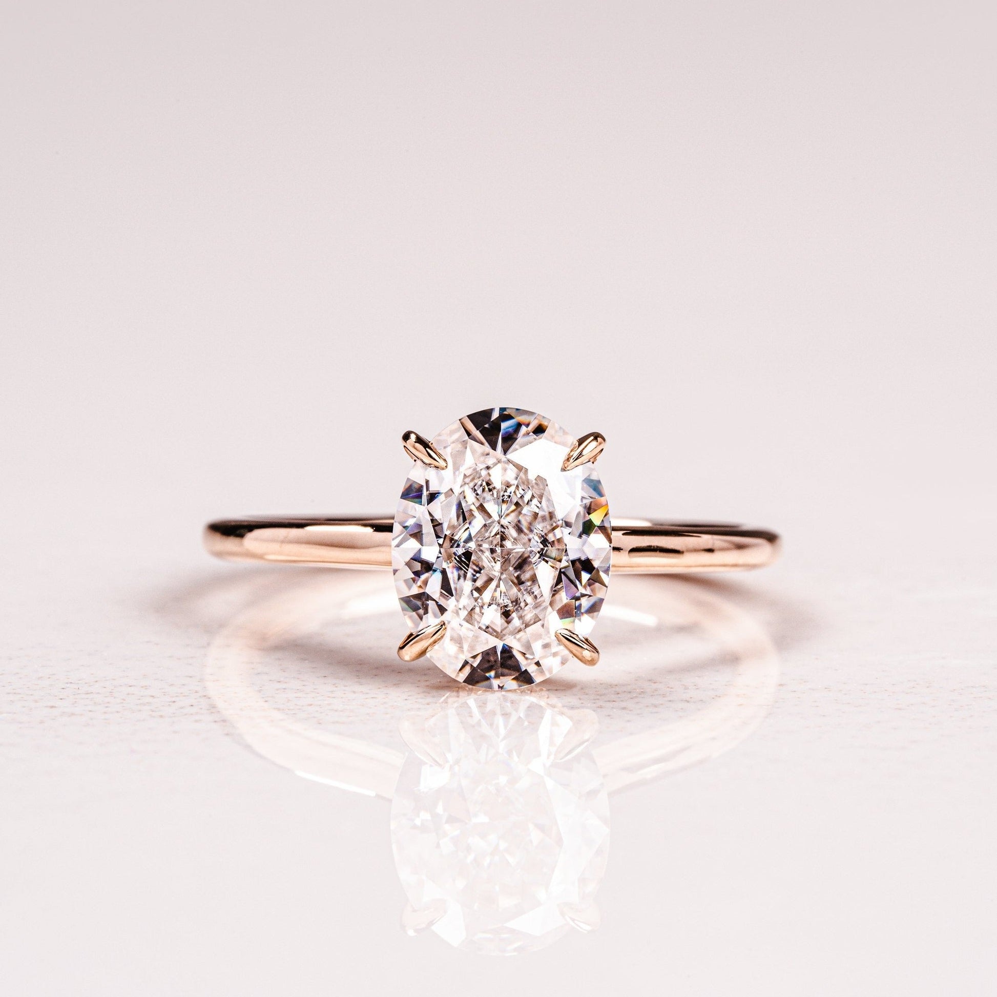 A solitaire engagement ring with a hidden halo setting, featuring an oval-cut moissanite gemstone on a gold band.