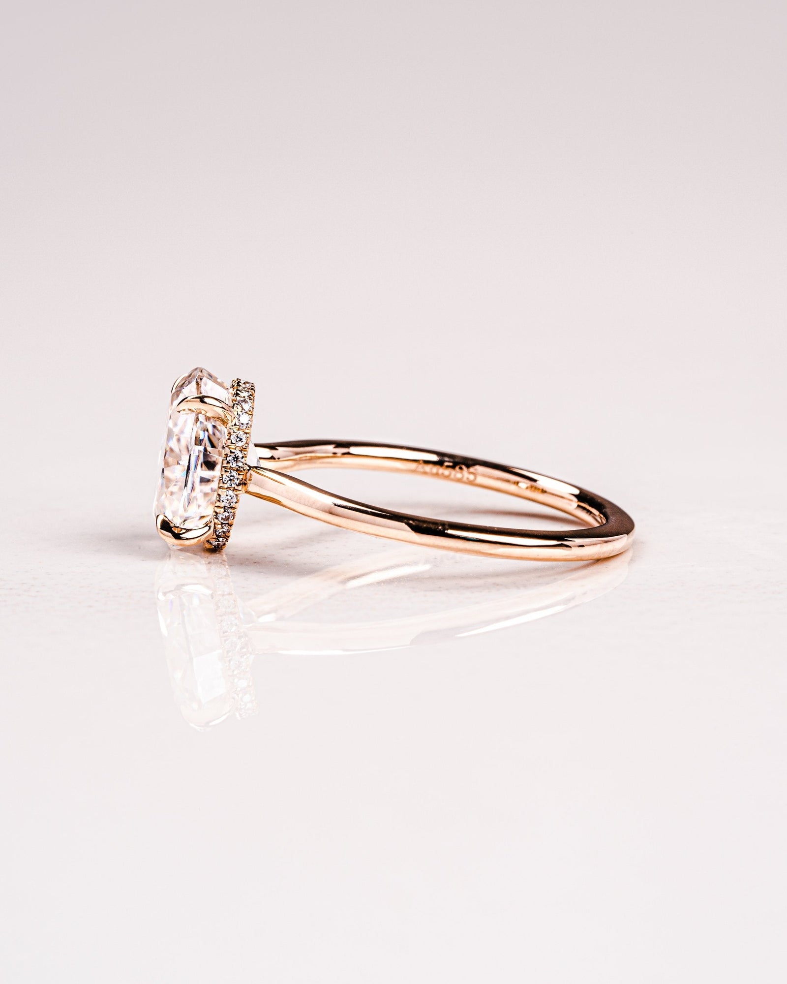 A solitaire engagement ring with a hidden halo setting, featuring an oval-cut moissanite gemstone on a gold band.