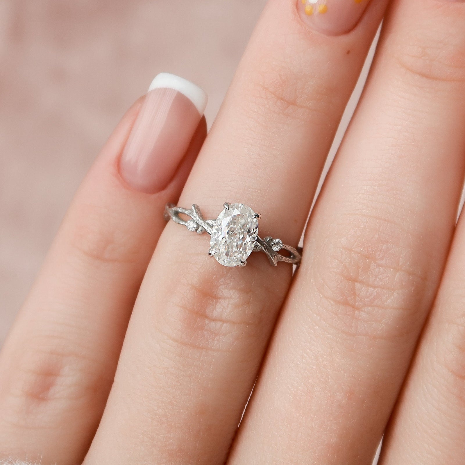 A woman's hand holding an oval-cut twig moissanite engagement ring with a gold band.