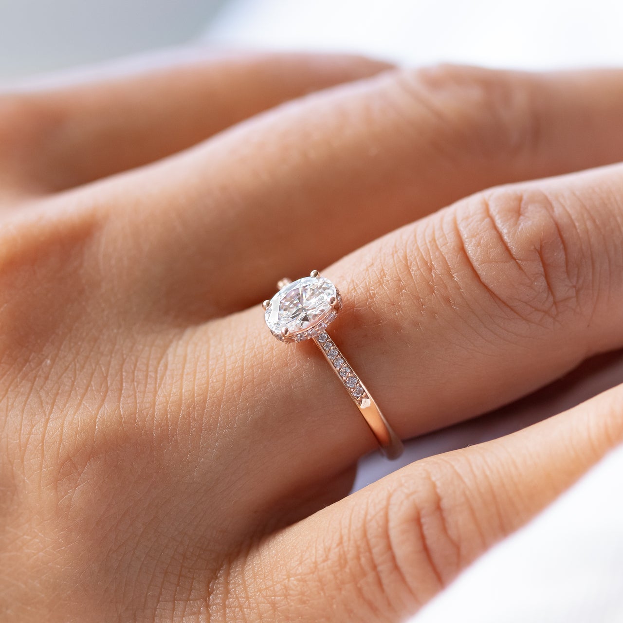 An oval-cut moissanite engagement ring with a hidden halo effect, set in a gold band, displayed on a white marble surface.